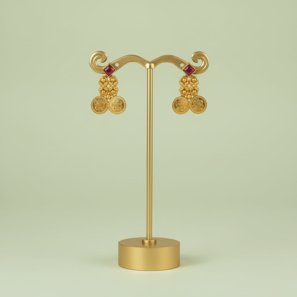 Gold earrings on a stand against a light green background
