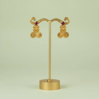 Gold earrings on a stand against a light green background