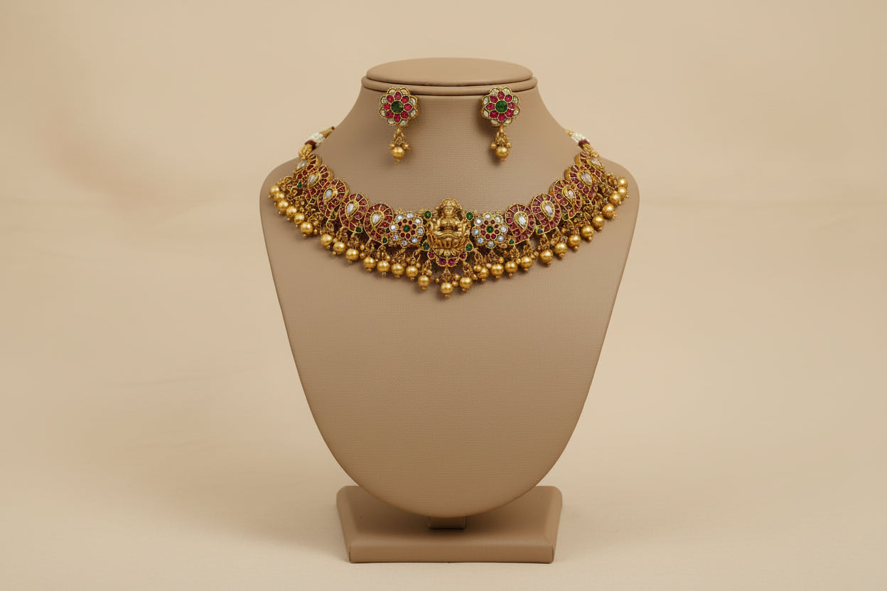 Gold necklace with red stones on a beige stand against a cream background