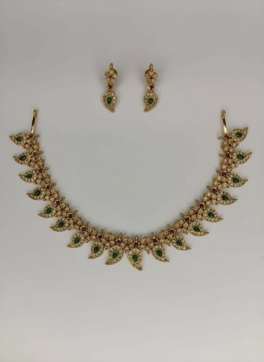 Gold necklace with green and red stones and matching earrings on a light gray background