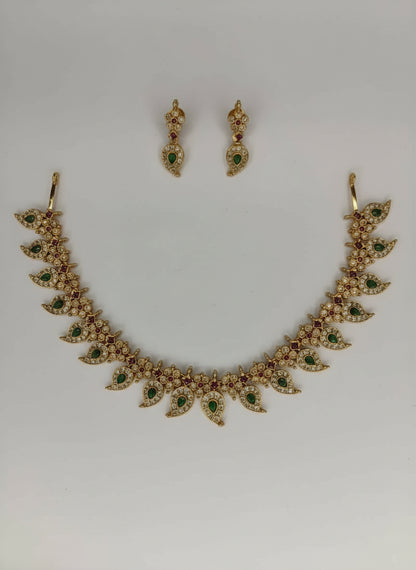 Gold necklace with green and red stones and matching earrings on a light gray background