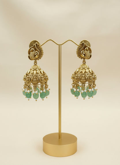 Gold earrings with green beads held in a hand against a blurred background
