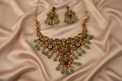 Gold necklace with green beads and matching earrings on a satin background