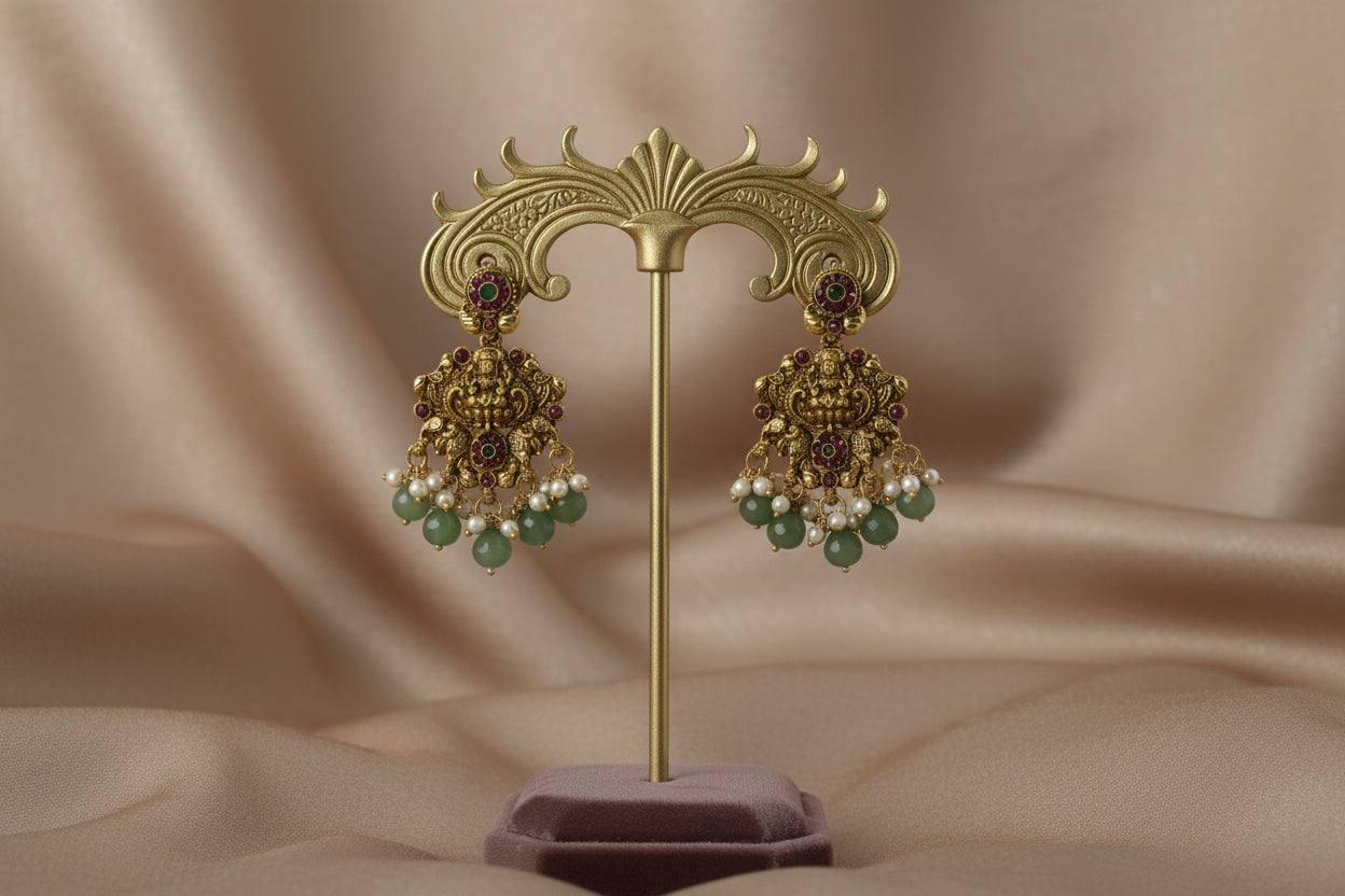 Ornate gold earrings with green and red gemstones on a beige background