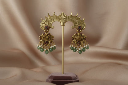 Ornate gold earrings with green and red gemstones on a beige background