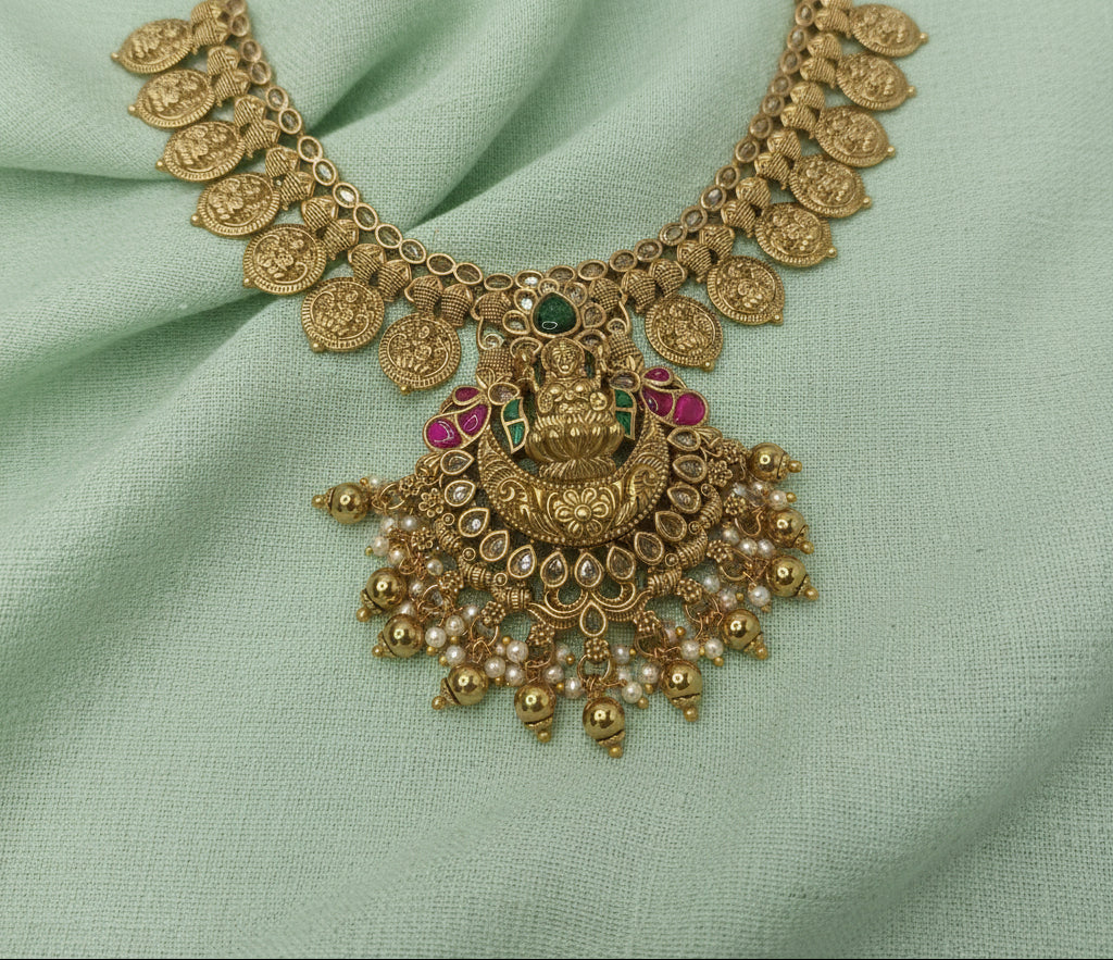 Ornate gold necklace with gemstones on a light green fabric background