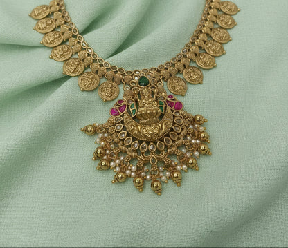 Ornate gold necklace with gemstones on a light green fabric background