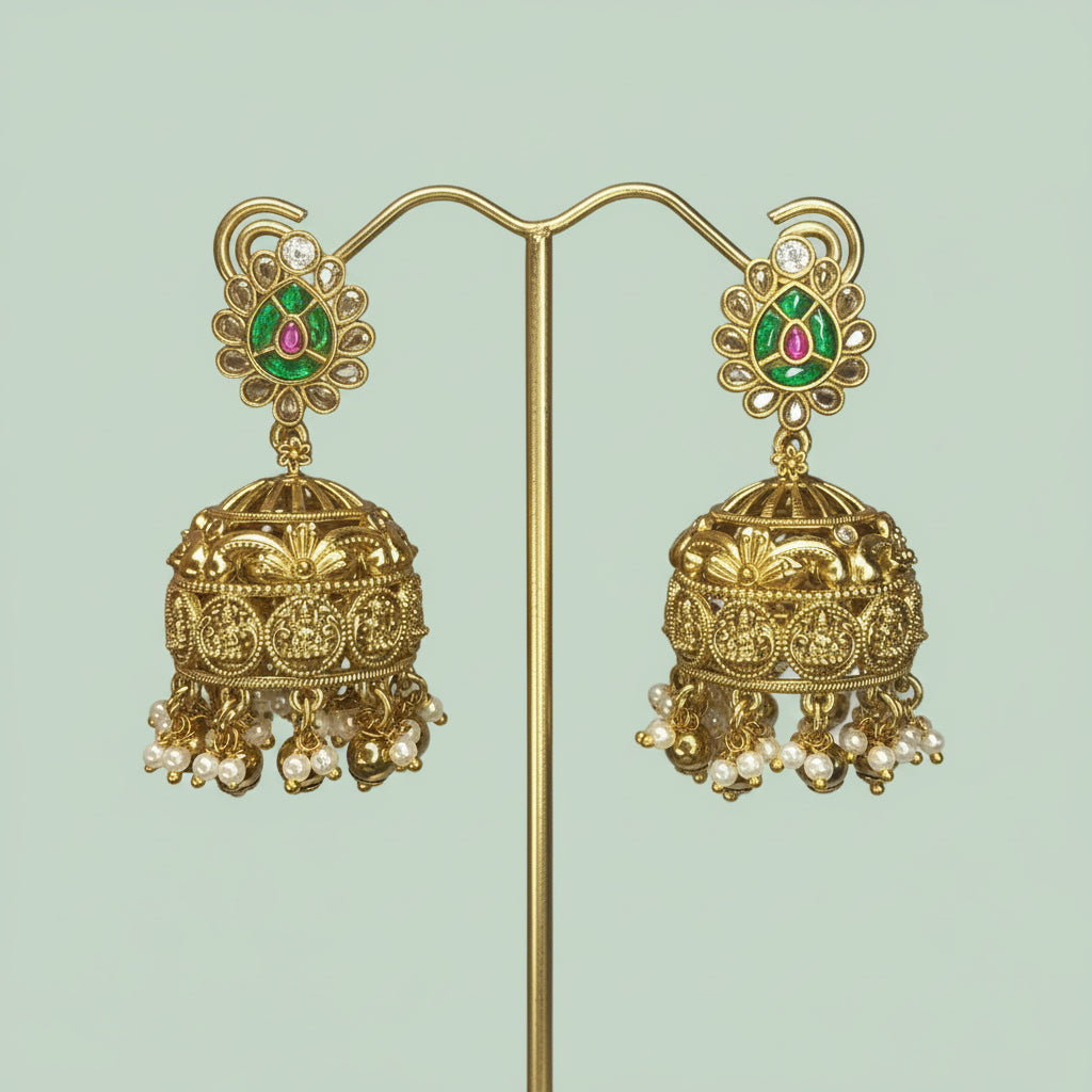 Ornate gold earrings with green and red gemstones on a light green background