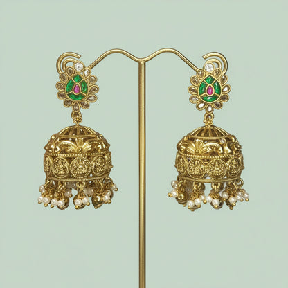 Ornate gold earrings with green and red gemstones on a light green background