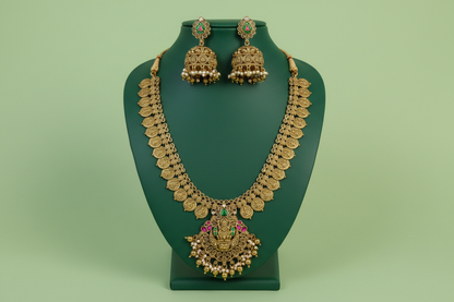 Gold necklace and earrings on a green stand against a green background