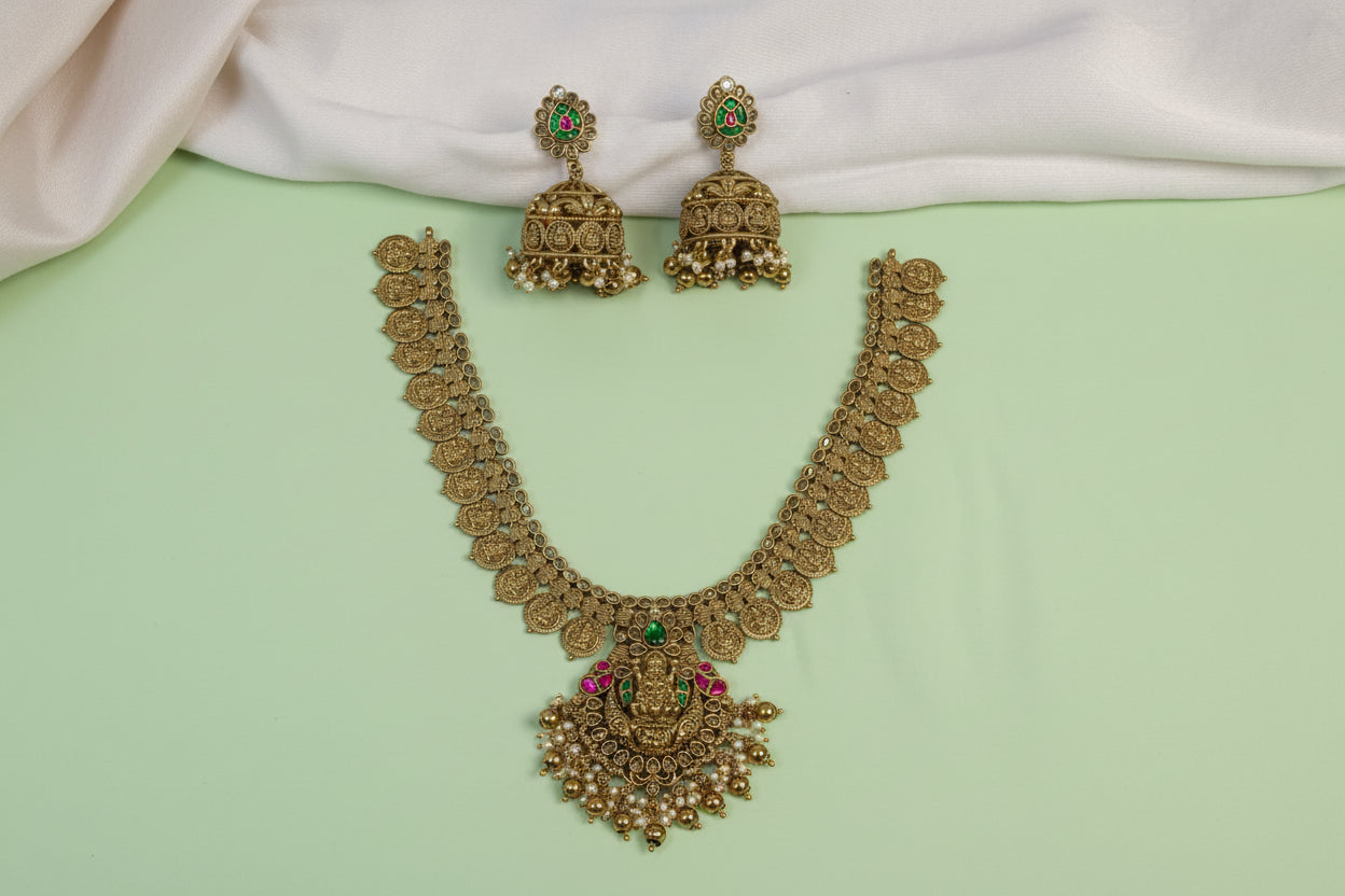 Gold necklace and earrings with green and red stones on a light green background