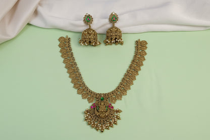 Gold necklace and earrings with green and red stones on a light green background