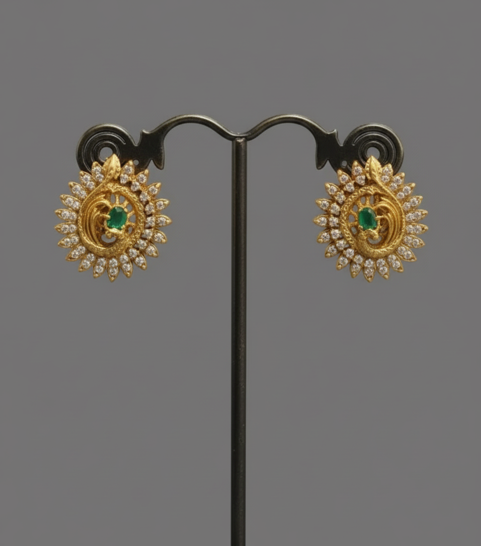 Gold earrings with green gemstones on a black stand against a gray background