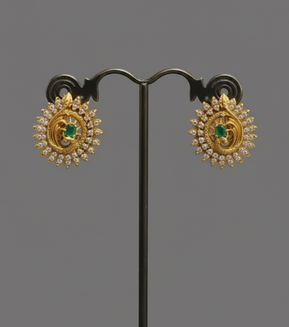 Gold earrings with green gemstones on a black stand against a gray background