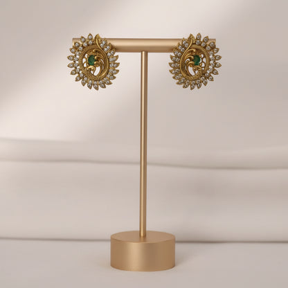 Pair of ornate earrings on a gold stand against a neutral background