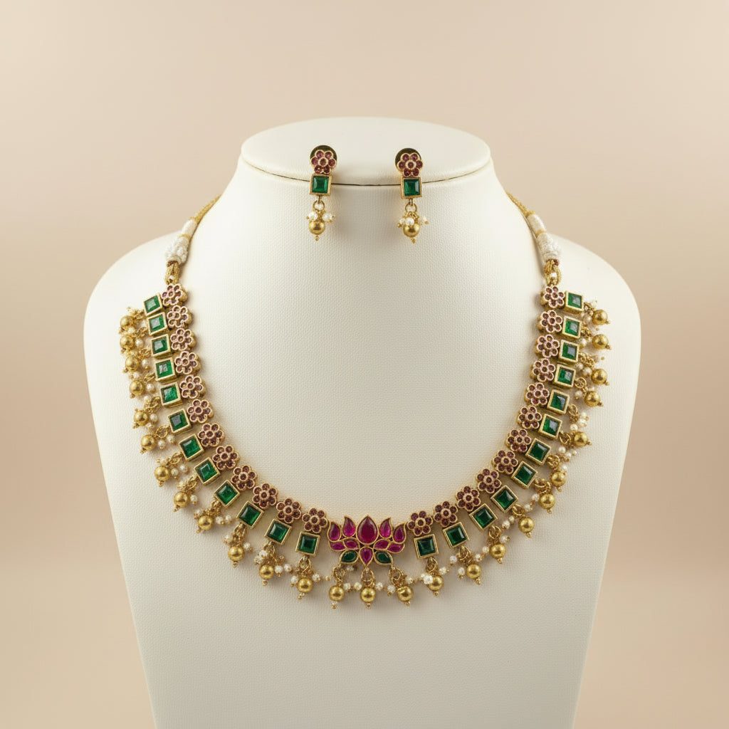 Gold necklace with green and red accents on a mannequin bust against a beige background