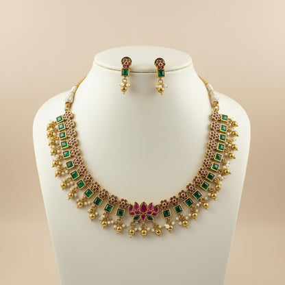 Gold necklace with green and red accents on a mannequin bust against a beige background