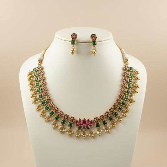 Gold necklace with green and red accents on a mannequin bust against a beige background