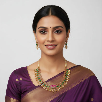 Gold necklace with green and red stones on a white fabric background