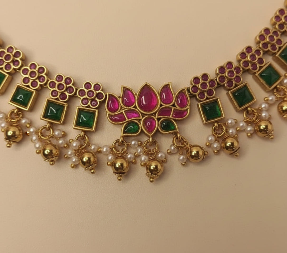 Ornate necklace with gold, green, pink, and pearl accents on a beige background