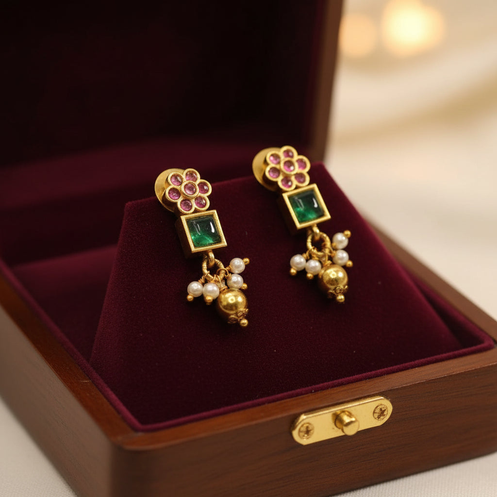 Gold earrings with gemstones and pearls on a burgundy velvet surface in a wooden box.