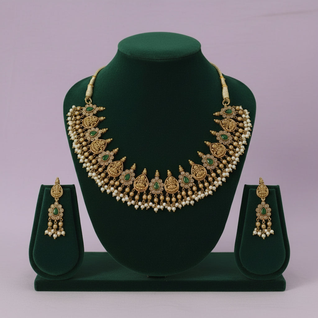Gold necklace with green stones and matching earrings on a green stand against a light purple background