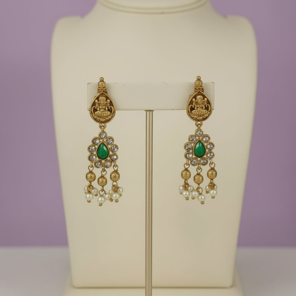 Gold and green earrings on a mannequin against a purple background