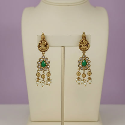 Gold and green earrings on a mannequin against a purple background