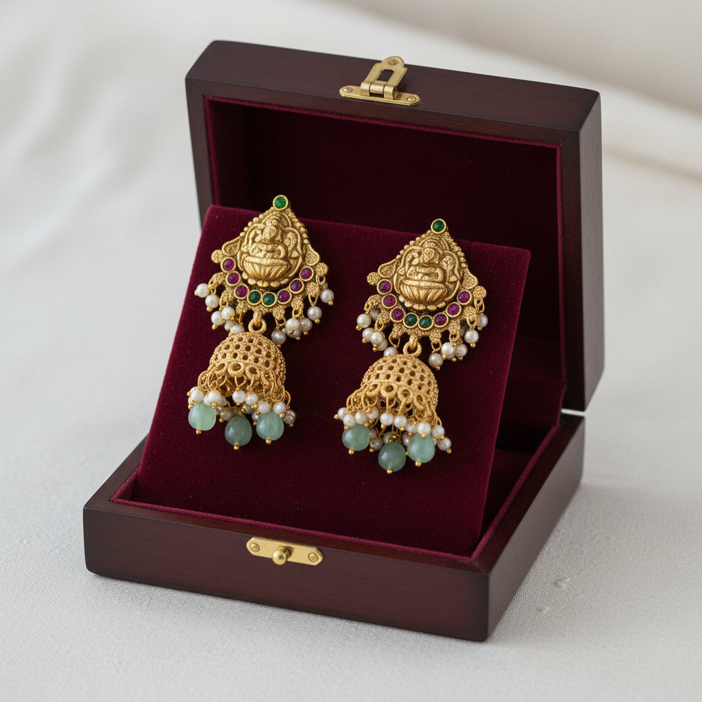 Ornate gold and green beaded necklace with matching earrings on a gray stand against a green background