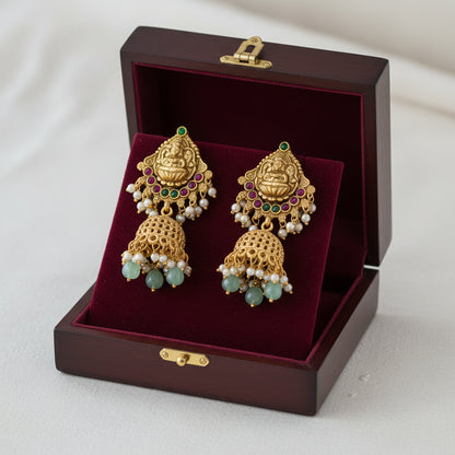 Ornate gold and green beaded necklace with matching earrings on a gray stand against a green background