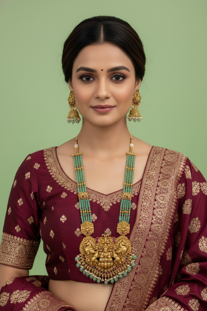 Woman wearing traditional maroon saree with gold and green jewelry against a light green background