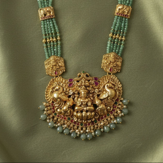 Ornate gold necklace with green beads on a green fabric background