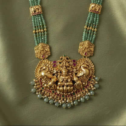 Ornate gold necklace with green beads on a green fabric background