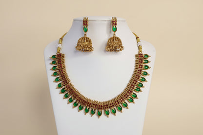 Gold necklace with green stones and matching earrings on a white stand against a beige background