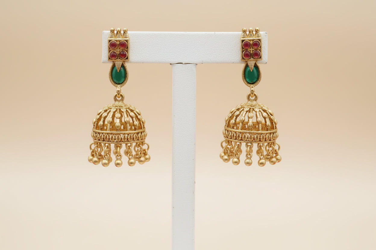 Gold earrings with red and green gemstones on a beige background