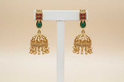 Gold earrings with red and green gemstones on a beige background