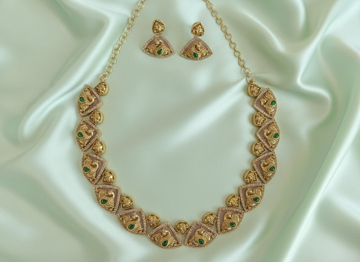 Gold necklace with green gemstones and matching earrings on a light green fabric background