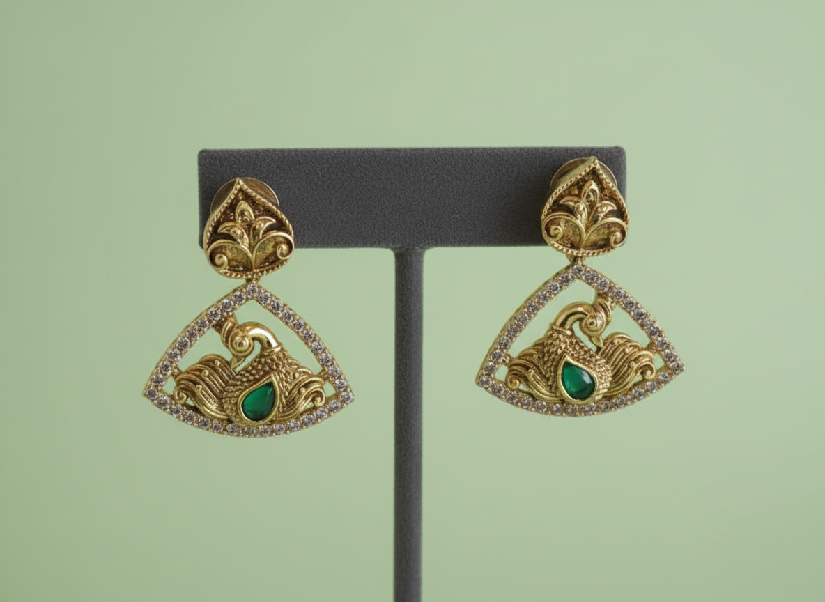 Gold and green earrings on a black stand against a light green background