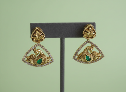 Gold and green earrings on a black stand against a light green background