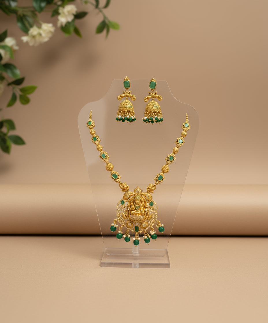 Gold necklace with green gemstones on a clear stand against a beige background