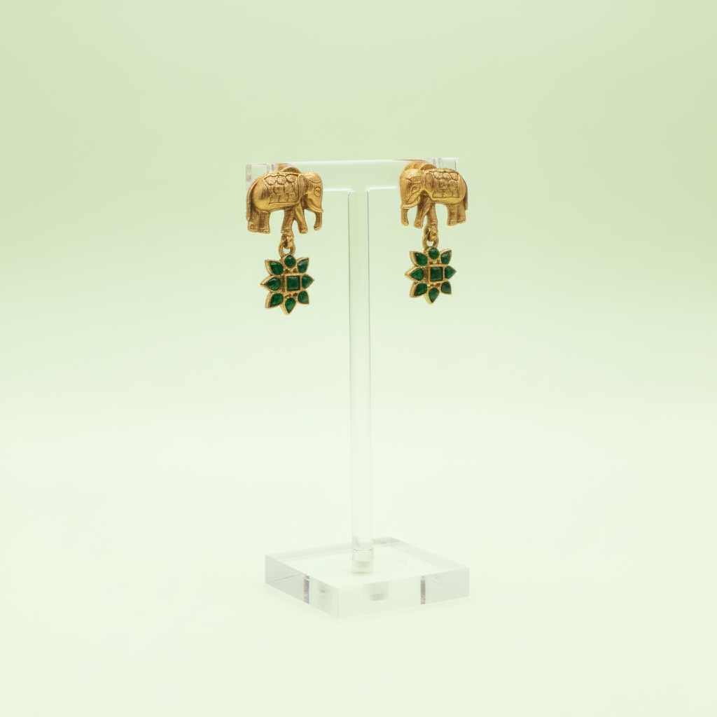 Gold elephant earrings with green gemstones on a light green background