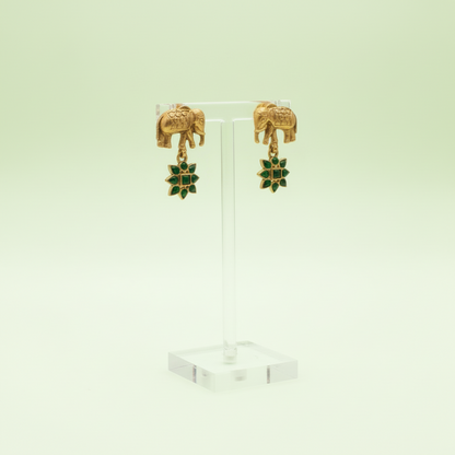 Gold elephant earrings with green gemstones on a light green background