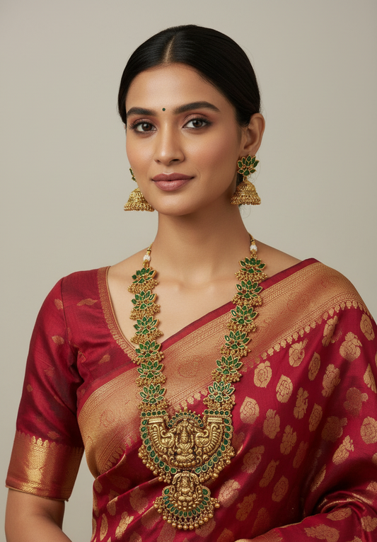 Woman wearing a traditional maroon saree with gold and green jewelry on a neutral background