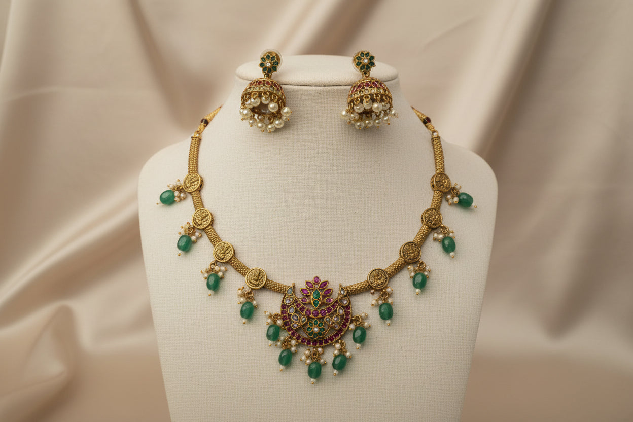Gold necklace with green gemstones and matching earrings on a beige fabric background