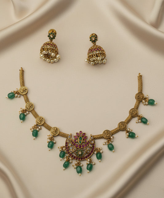 Gold necklace with green gemstones and matching earrings on a beige fabric background