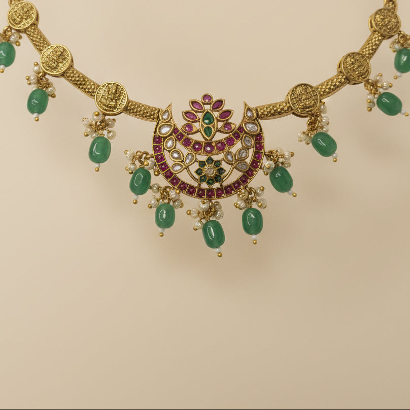 Gold necklace with green gemstones and red stones on a gray background