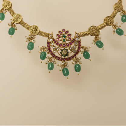 Gold necklace with green gemstones and red stones on a gray background
