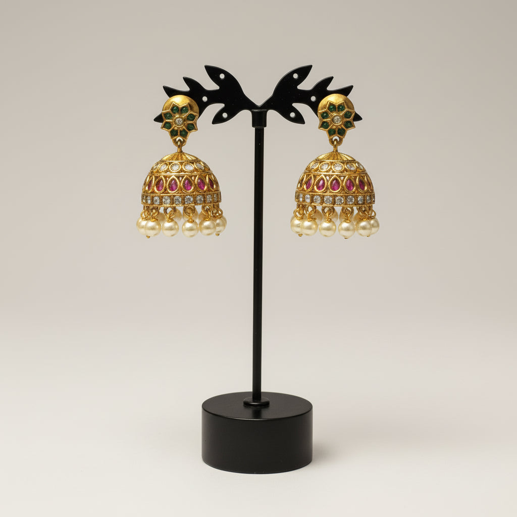 Gold and pearl earrings on a black stand against a light gray background