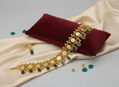 Gold necklace with green stones on a red pillow and beige fabric background