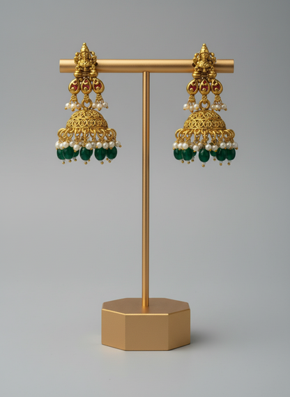 Gold earrings with green and pearl accents on a gold stand against a gray background